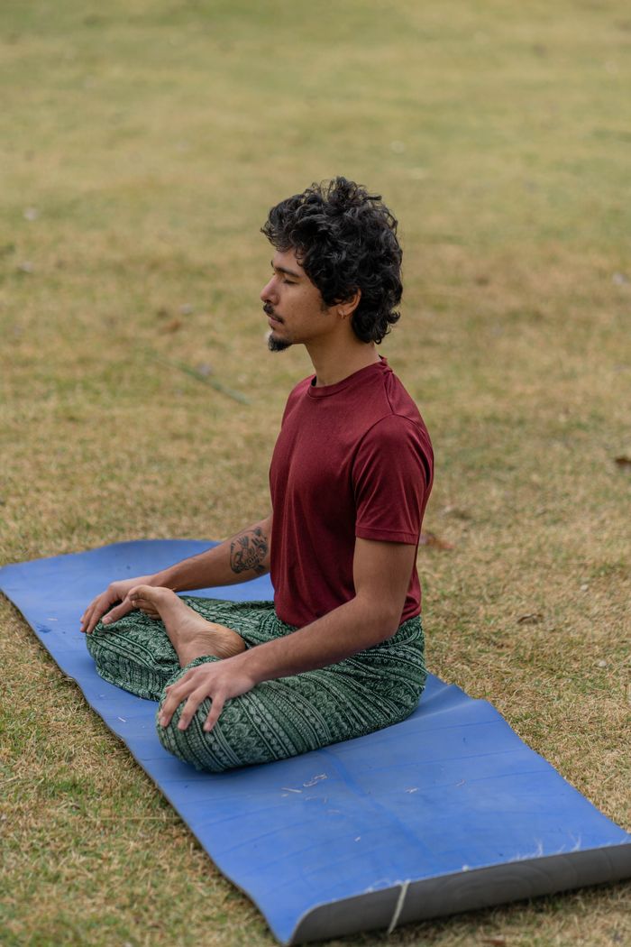 services-03 A man meditating in a relaxed posture on a blue yoga mat in a grassy field.